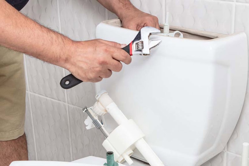 How to Unclog Your Slow-Draining Toilet. Close up photo of a person performing maintenance on a toilet.
